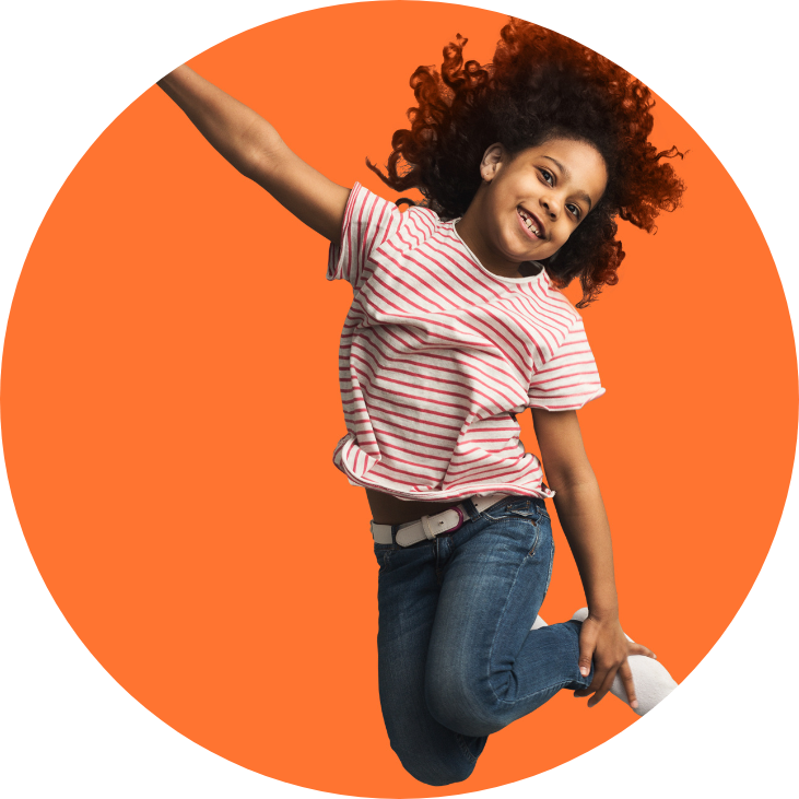 Girl in a red stripped shirt jumping and holding her feet in front of an orange background.