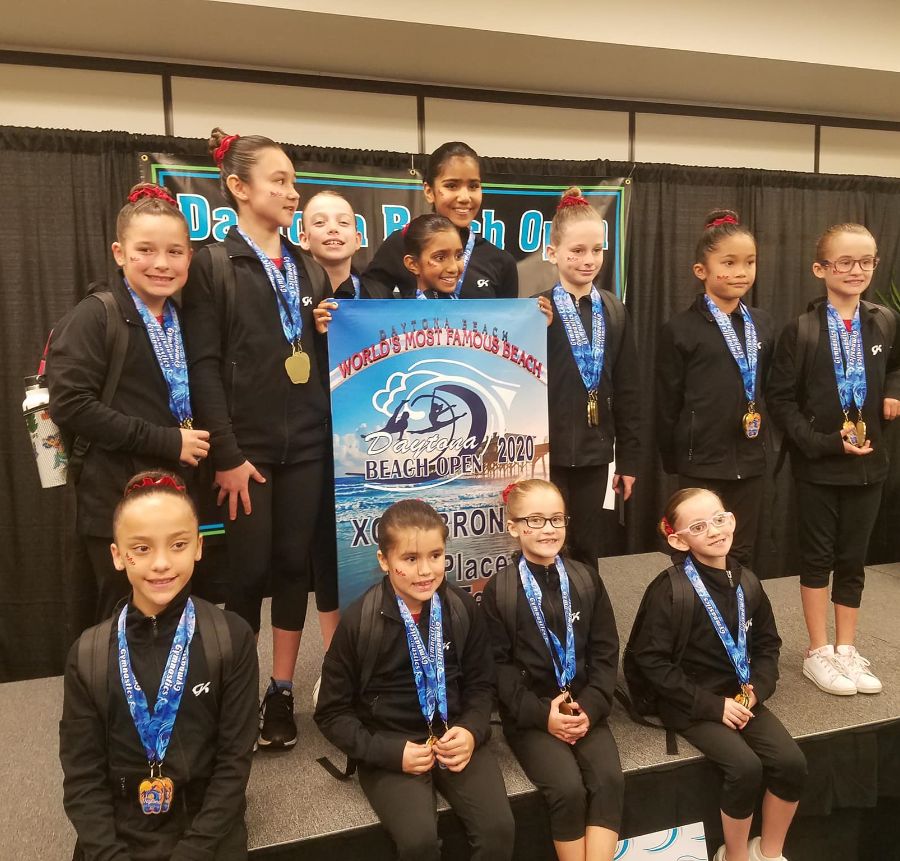Rad Gymnastics students pose on stage with their medals and Daytona Beach Open poster.
