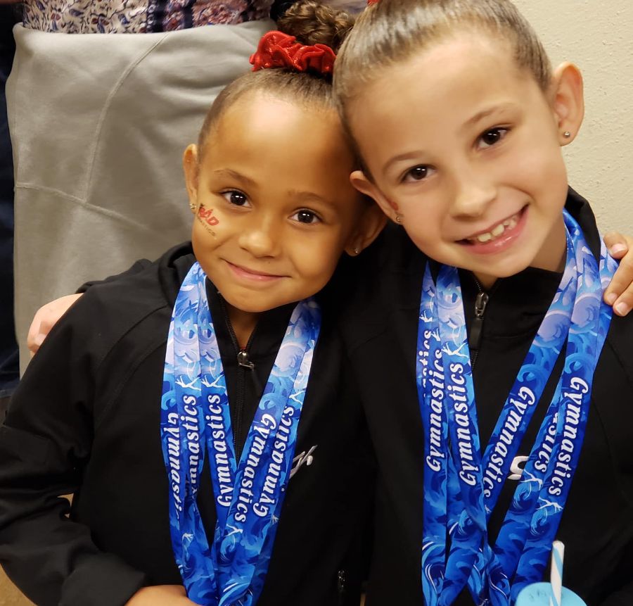 Two girls wear blue medals around their neck after winning their gymnastics competition.